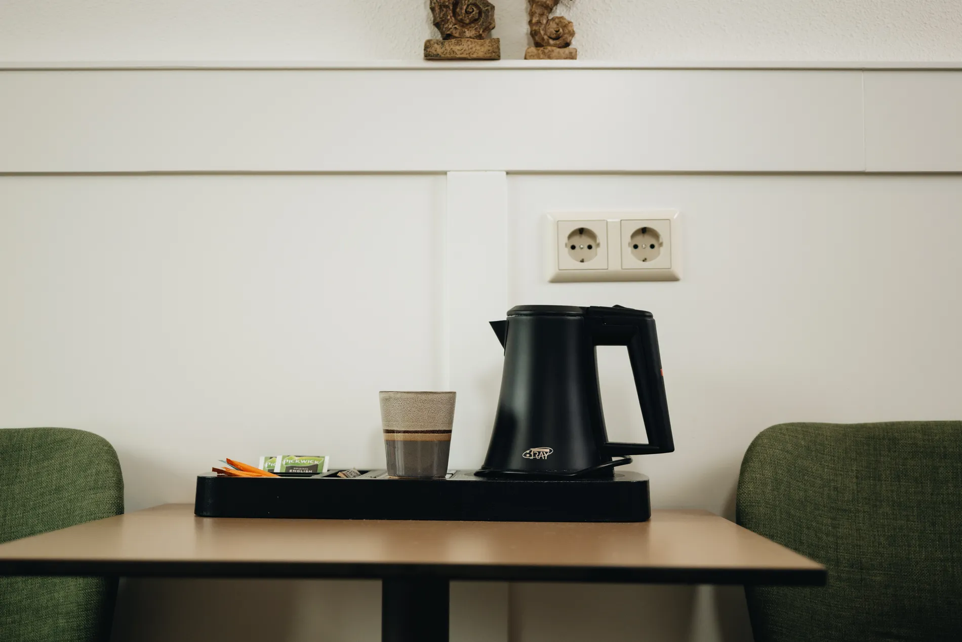 Detail van het koffie- en theestation op de hotelkamer met een moderne zwarte waterkoker en welkomstassortiment.